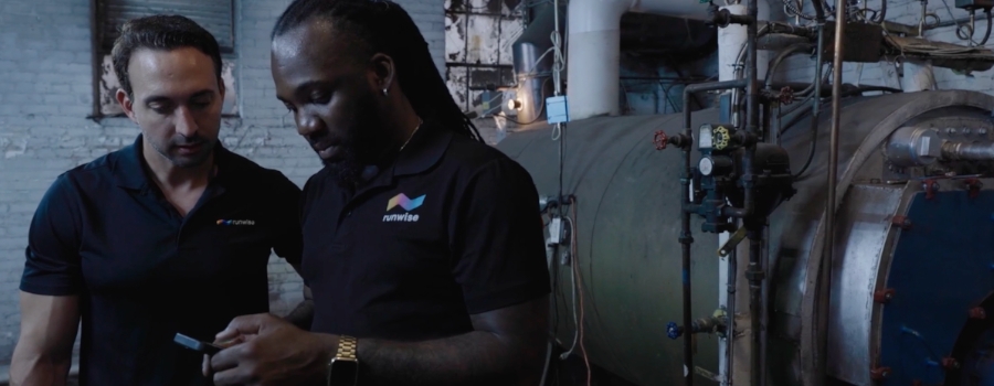 Two Runwise technicians checking a mobile device inside a boiler room with large machinery