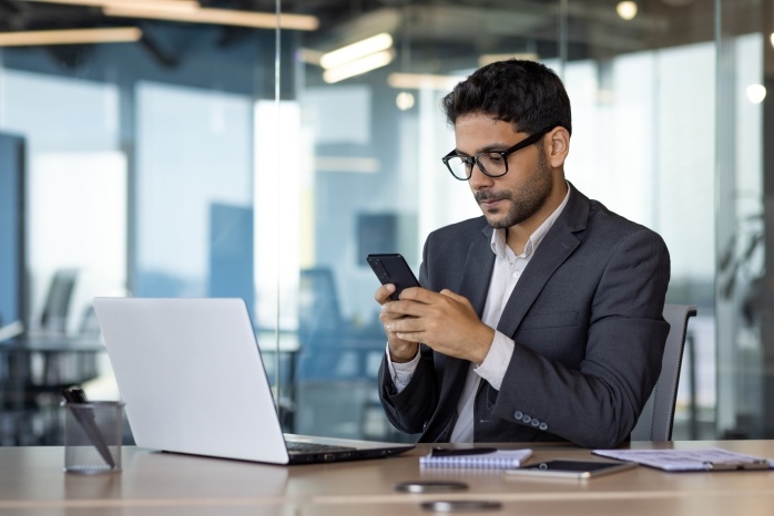 Tile|Businessman looking at smartphone with laptop
