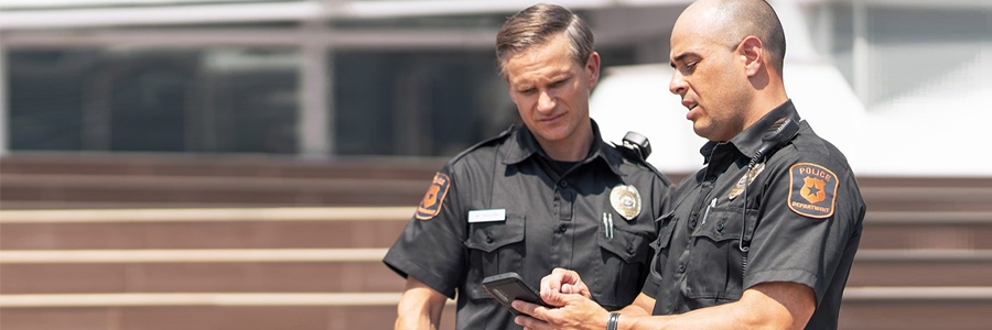 Full|Two police officers using a smartphone while standing outside of police precinct