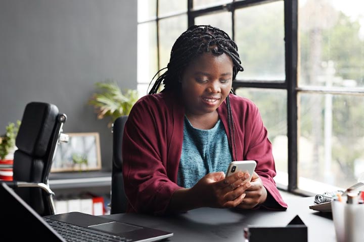 Full|Woman in office by window looking at her phone