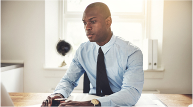 Wide|Man sitting at desk using laptop wearing blue shirt