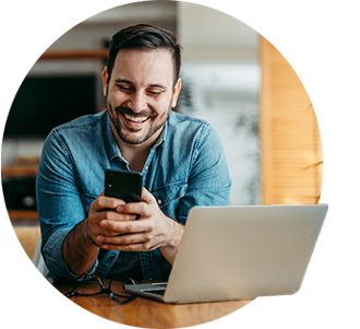 Man looking at his phone in front of his laptop.