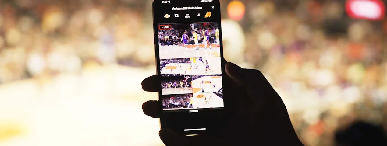 Hand holding a smartphone while watching basketball game