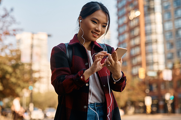 Tile|Young Asian student texting on her smart phone in city.
