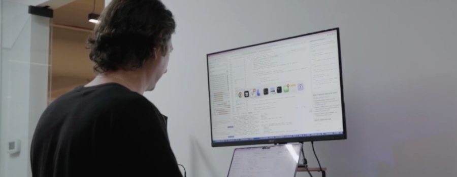 Man working on a large monitor displaying software code and application icons