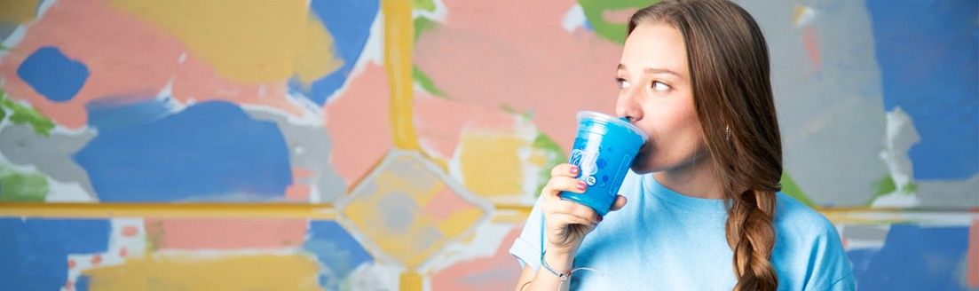 Thin | Young Woman Drinking Blue Beverage Against Colorful Mural