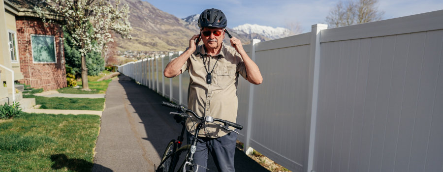 Wide|Active senior man wearing a helmet and medical alert device while standing with a bicycle