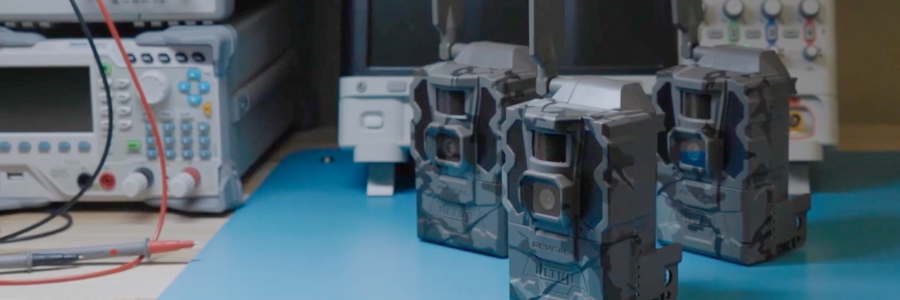 Three camouflaged Tactacam cameras standing on an electronics workbench